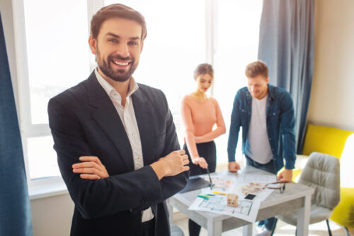 Smiling male mortgage officer at office with a couple in background - 5 Mortgage Lending Strategies to Help Your Customers | DG Pinnacle TPO | Miami Wholesale Mortgage Funding Lender
