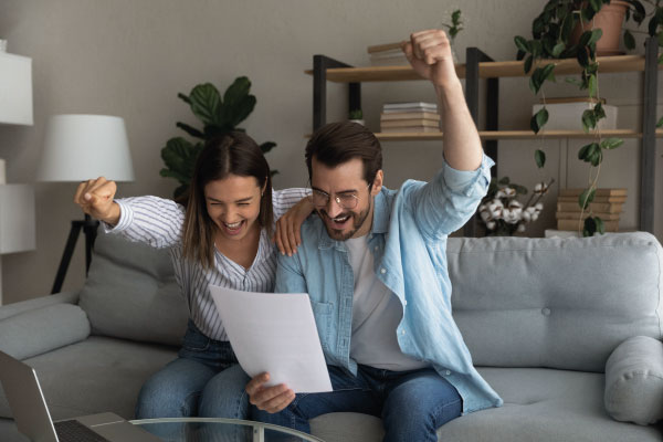 Happy young couple having some good news sitting on their couch | Who is eligible for Non-QM Loans | DG Pinnacle TPO - Miami Wholesale Mortgage Lender