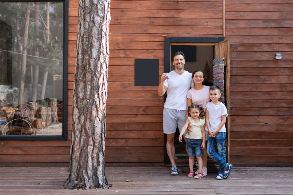 Young happy couple standing in front of their country house with their kids - USDA Matrix Mortgage Loans | DG Pinnacle TPO - Wholesale Division | Miami Mortgage Lender