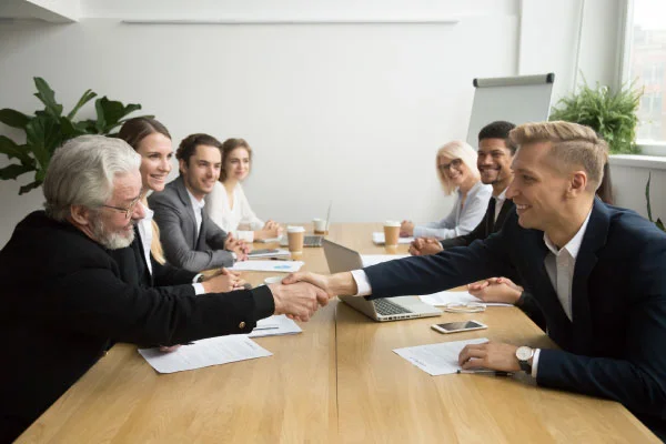 Group of people having a meeting and two of them shaking hands over the desk | MBA urges federal rollback of mortgage rules | DG Pinnacle TPO - Wholesale Division | Miami Mortgage Lender