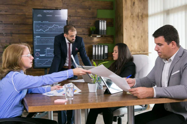 A woman handing a document to a man and two more people discussing on the background | MBA urges federal rollback of mortgage rules | DG Pinnacle TPO - Wholesale Division | Miami Mortgage Lender