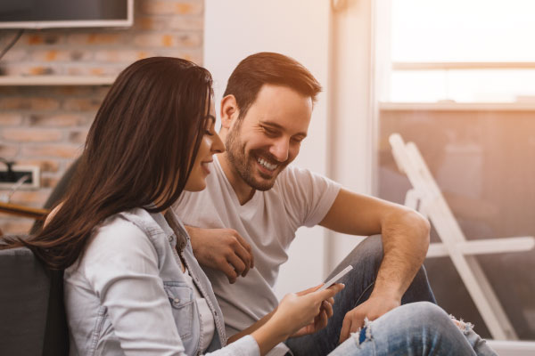 Happy young couple sitting on their couch and smiling for being approved for a mortgage loan | DG Pinnacle TPO - Miami Wholesale Mortgage Funding Lender